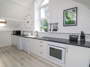 A kitchen with white cabinets black countertop a window a wall clock and utensils at The Old Workshop in Dre-Fach near Lampeter