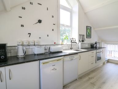 A kitchen with white cabinets black countertop a wall clock and appliances at The Old Workshop in Dre-Fach near Lampeter