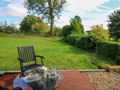A garden with grass and trees and a glass table with a teapot and cups on a wooden patio at The Old Workshop in Dre-Fach near Lampeter