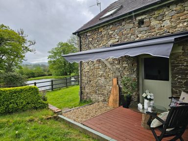 A stone house with a small patio with chairs and a table overlooking a garden and pond at The Old Workshop in Dre-Fach near Lampeter