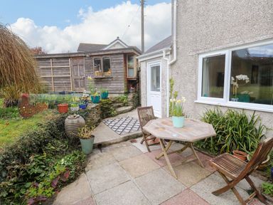 A small garden patio with a wooden table and two chairs next to a house and a wooden shed in the background at Elder Cottage Studio in Perranwell Station near Ponsanooth