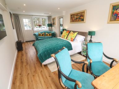 A bedroom with a bed sofa chairs and paintings at Elder Cottage Studio in Perranwell Station near Ponsanooth