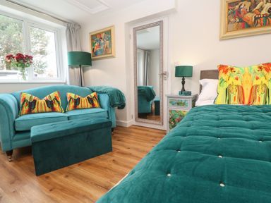A bedroom with teal sofa bed pillows and bedspread wooden floor and a large floor mirror at Elder Cottage Studio in Perranwell Station near Ponsanooth