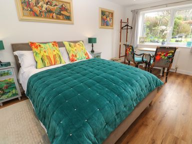 A bedroom with a bed green comforter art on walls two chairs and a desk by window at Elder Cottage Studio in Perranwell Station near Ponsanooth