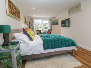 A bedroom with a double bed a bedside table with lamp two chairs and a table by the window and a wall mounted tv at Elder Cottage Studio in Perranwell Station near Ponsanooth
