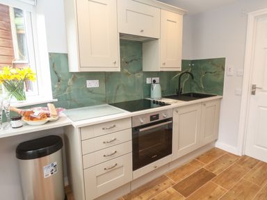 A kitchen with beige cabinets green marble backsplash and wooden floor at Elder Cottage Studio in Perranwell Station near Ponsanooth