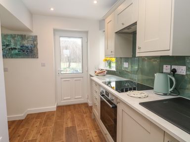 A kitchen with wooden floor cabinets a stove oven kettle and a door at Elder Cottage Studio in Perranwell Station near Ponsanooth