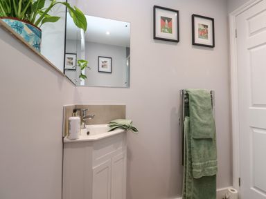 A bathroom with a white sink cabinet green towels on a chrome towel rack a mirror and framed pictures on the wall at Elder Cottage Studio in Perranwell Station near Ponsanooth