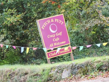 An outdoor sign for a pitch and putt golf course with colorful flags and trees in the background at Elder Cottage Studio in Perranwell Station near Ponsanooth