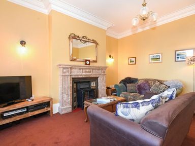 A living room with a fireplace a mirror above a mantle a television on a wooden stand two sofas and framed pictures on the wall at Claremount in Alnmouth