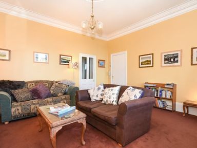 A living room with two sofas a coffee table bookshelves and framed pictures on yellow walls at Claremount in Alnmouth