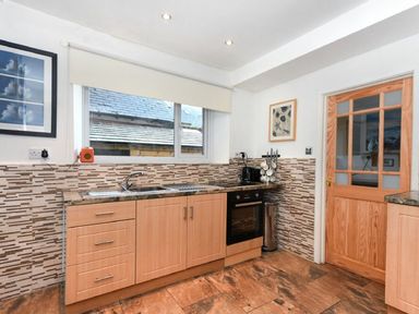 A kitchen with wooden cabinets a sink oven and a window with a blind at Claremount in Alnmouth
