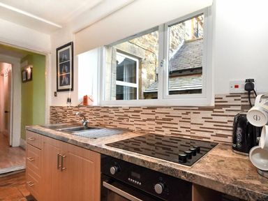 A kitchen with a marble countertop electric stovetop under a window with stone building outside at Claremount in Alnmouth