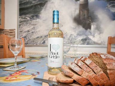 A dining table with sliced bread and a bottle of Pinot Grigio wine with wine glasses at Claremount in Alnmouth