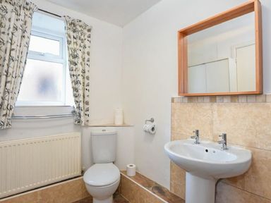 A bathroom with a toilet sink mirror and a window with patterned curtains at Claremount in Alnmouth