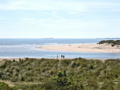 A beach with grassy dunes and four people standing near water at Claremount in Alnmouth