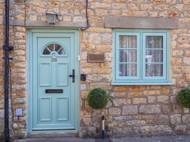 Stone exterior wall with a light blue front door numbered 30 and matching window with lace curtains at 30 Fleet Street in Beaminster