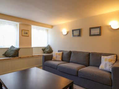 A living room with a gray sofa a dark coffee table and windows with cushions at 30 Fleet Street in Beaminster