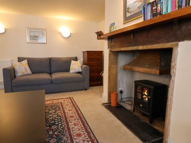 A living room with a grey sofa a wooden chest of drawers and a wood stove in the fireplace at 30 Fleet Street in Beaminster