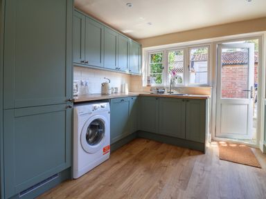 A kitchen with green cabinets a washing machine a wooden countertop a sink and a door leading outside at 30 Fleet Street in Beaminster