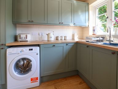 A kitchen with green cabinets washing machine toaster kettle and a window at 30 Fleet Street in Beaminster