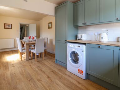 A kitchen and dining area with green cabinets white appliances and a wooden dining table with chairs at 30 Fleet Street Beaminster