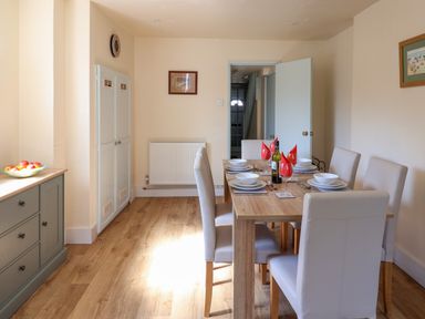 A dining room with a wooden table set for six with red napkins and white chairs at 30 Fleet Street in Beaminster