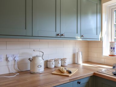 A kitchen countertop with a kettle, canisters, cutting board with bread and knife next to a window at 30 Fleet Street in Beaminster