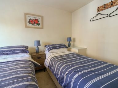 A bedroom with two single beds with striped bedding two bedside tables with lamps a framed flower picture and a wall-mounted coat rack with hangers at 30 Fleet Street in Beaminster