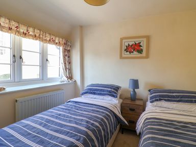 A bedroom with two single beds with striped bedding a wooden bedside table with a blue lamp and a window with floral curtains at 30 Fleet Street in Beaminster