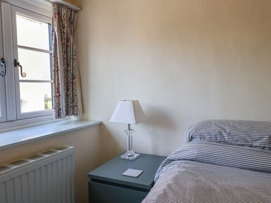 A bedroom corner with a window with floral curtains a bedside table with a lamp and a bed with striped linens at 30 Fleet Street in Beaminster