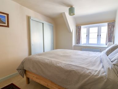 A bedroom with a bed near a window with curtains and a closet with sliding doors at 30 Fleet Street in Beaminster
