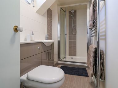 A bathroom with a toilet, sink with counter, shower enclosure, towel rack with towels and a opened door at 30 Fleet Street in Beaminster