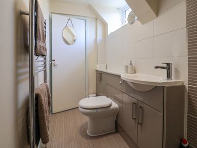 A bathroom with a toilet sink and cabinets with towels hanging on a rail and a round mirror on the door at 30 Fleet Street in Beaminster