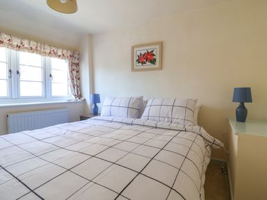 A bedroom with a double bed with checkered bedding two blue lamps on bedside tables and a window with floral curtains at 30 Fleet Street in Beaminster