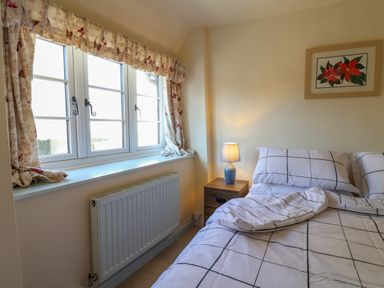 A bedroom with a bed with checkered bedding a bedside table with a lamp a window with floral curtains and a framed flower picture on the wall at 30 Fleet Street Beaminster