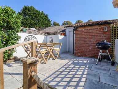 A paved outdoor patio with wooden table and chairs a barbecue grill and a brick shed at 30 Fleet Street in Beaminster