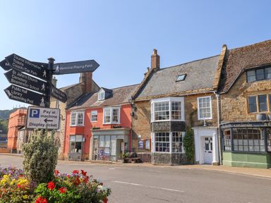Street view with old buildings directional signs and flowers in a planter at 30 Fleet Street in Beaminster