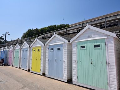 A row of small beach huts with pastel colored doors by a concrete walkway at 30 Fleet Street in Beaminster