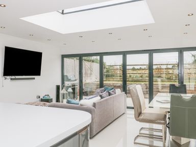 A living area with a sofa dining table chairs and a wall-mounted television near glass doors at Orchard Leigh in North Petherton