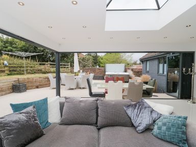 A living room with a gray sofa and cushions facing an outdoor patio with dining table chairs and a hot tub at Orchard Leigh in North Petherton