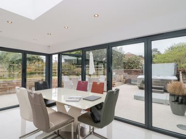 A dining room with a table and six chairs next to glass sliding doors showing an outdoor patio and garden at Orchard Leigh in North Petherton