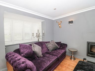 A living room with a purple sofa gray cushions white window shutters and a small silver side table at Orchard Leigh in North Petherton