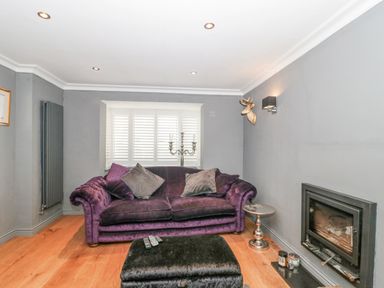 A living room with a purple sofa gray walls a fireplace and a small round table at Orchard Leigh in North Petherton
