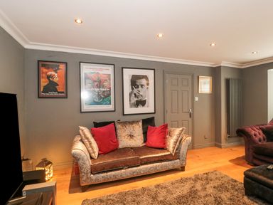 A living room with a sofa with red and beige cushions and framed pictures on the wall at Orchard Leigh in North Petherton