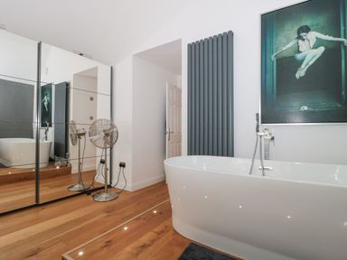 A bathroom with a freestanding bathtub wooden floor mirrored wardrobe and a floor fan at Orchard Leigh in North Petherton