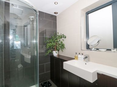 A bathroom with a corner shower cubicle a white sink with toiletries a mirror a window and a plant on a cabinet at Orchard Leigh in North Petherton