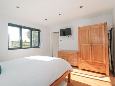 A bedroom with a wooden bed, wardrobe, dresser, and wall-mounted TV at Orchard Leigh in North Petherton