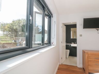 A room with large windows showing an outdoor area and an open door leading to a bathroom with black wall panels at Orchard Leigh in North Petherton