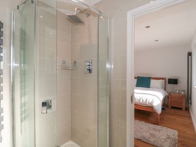 A shower with glass doors adjacent to a bedroom with a wooden bed and nightstand at Orchard Leigh in North Petherton